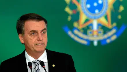 HD desktop wallpaper of a man in a suit and tie speaking at a podium, with the Brazilian national emblem blurred on a green background.