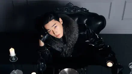 K-pop ATEEZ-inspired black 4K desktop wallpaper: solitary figure in glossy black coat with fur collar reclining at a candlelit table, moody high-contrast portrait.