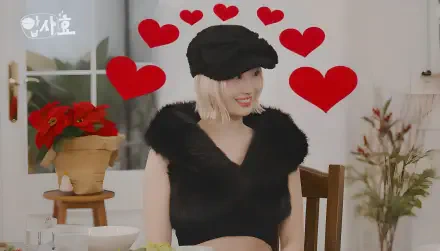 K-pop idol smiling on a live-show set, blonde bob in a black cap and cropped fuzzy top, red heart graphics floating above; 4K Ultra HD desktop wallpaper background.