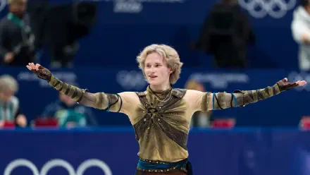 Ice skater in an ornate costume, arms outstretched on the Winter Olympics rink — dynamic sports action captured as a 2K Quad HD PC desktop wallpaper background.