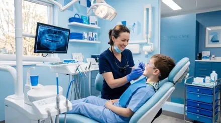 5K Ultra HD PC desktop wallpaper/background: dentist smiling while treating a young patient in a modern dental clinic, bright blue treatment room with an x-ray monitor.