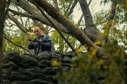 4K Ultra HD PC desktop wallpaper: a scene from Apex (2026) showing a lead actor perched in trees, aiming a crossbow over a rocky outcrop.