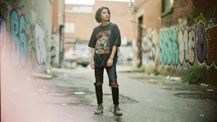 Soft grunge 4K Ultra HD PC Desktop Wallpaper and Background: solitary person in ripped jeans and a band tee stands in a graffiti-lined urban alley, muted colors and hazy film-like light.