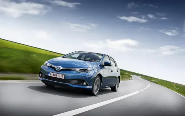 Blue Toyota Auris hatchback on a winding road under a dramatic cloudy sky — 2K Quad HD PC desktop wallpaper and background.