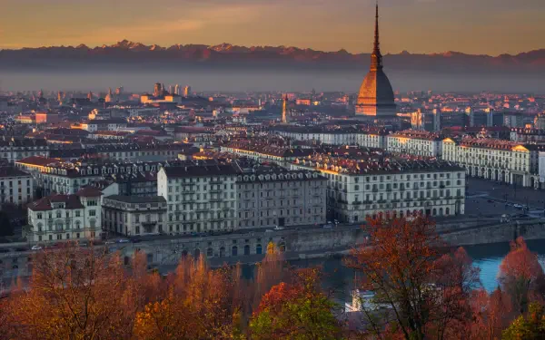 4K Ultra HD PC wallpaper of hazy Turin, Italy cityscape at dusk — Mole Antonelliana rising above riverfront buildings with warm lights and autumn foliage.