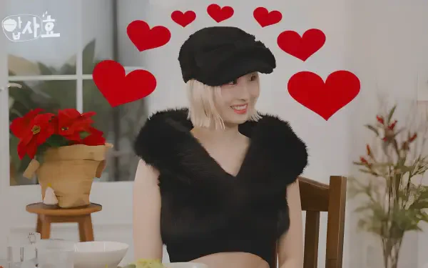 K-pop idol smiling on a live-show set, blonde bob in a black cap and cropped fuzzy top, red heart graphics floating above; 4K Ultra HD desktop wallpaper background.