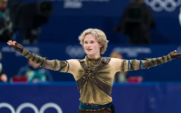 Ice skater in an ornate costume, arms outstretched on the Winter Olympics rink — dynamic sports action captured as a 2K Quad HD PC desktop wallpaper background.