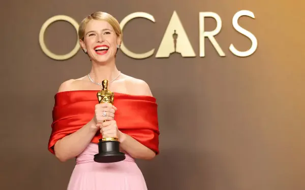 Young woman in red off-shoulder gown smiling while holding an Oscar statuette in front of an Oscars backdrop — 4K Ultra HD PC desktop wallpaper