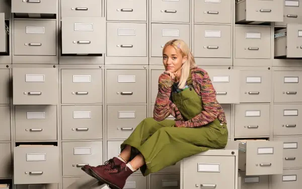 HD PC desktop wallpaper for the TV show High Potential: a young woman in green overalls sits on a filing cabinet amid rows of drawers, smiling thoughtfully.