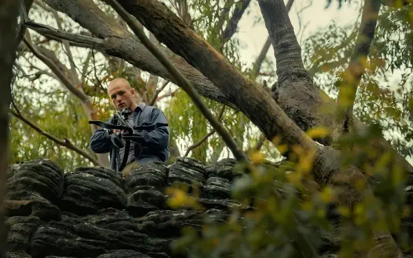 4K Ultra HD PC desktop wallpaper: a scene from Apex (2026) showing a lead actor perched in trees, aiming a crossbow over a rocky outcrop.