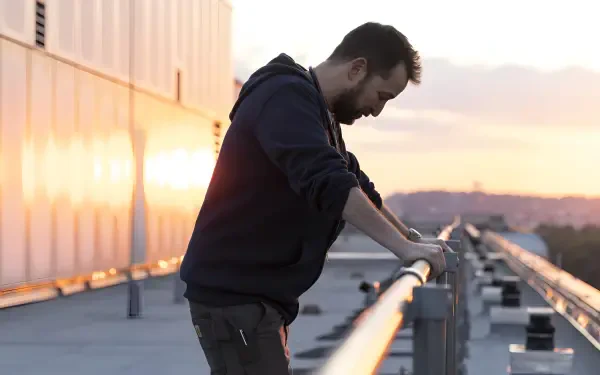 4K PC wallpaper from TV show The Pitt: solitary male actor leans on a rooftop railing at sunset, reflective and moody atmosphere.