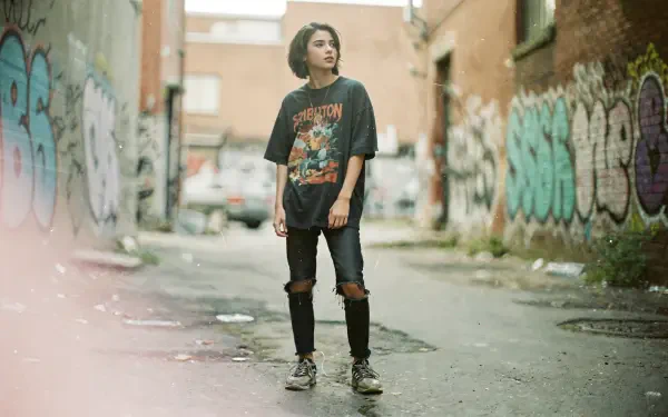 Soft grunge 4K Ultra HD PC Desktop Wallpaper and Background: solitary person in ripped jeans and a band tee stands in a graffiti-lined urban alley, muted colors and hazy film-like light.