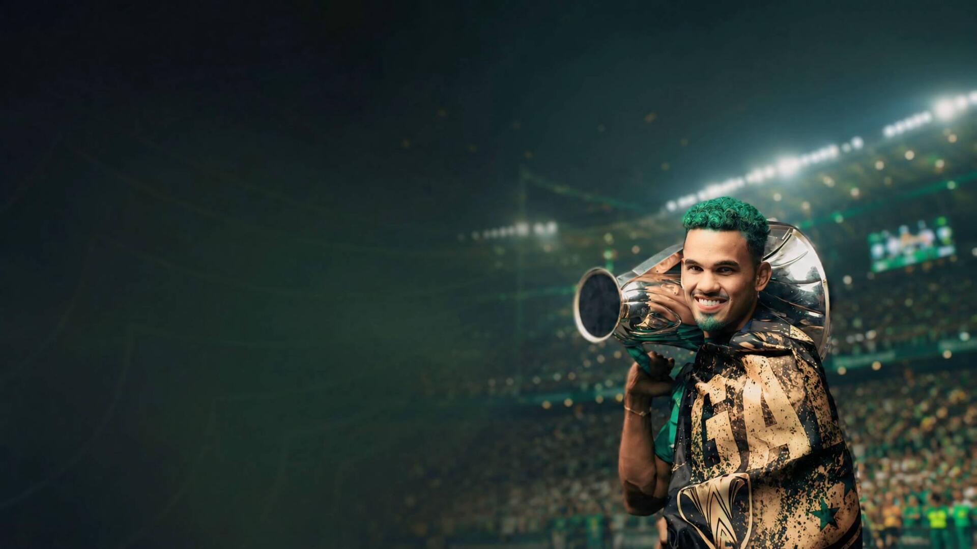HD PC desktop wallpaper of an Al Ahli Saudi Pro League player in club green, smiling and holding a trophy-like megaphone amid stadium lights and a cheering crowd.