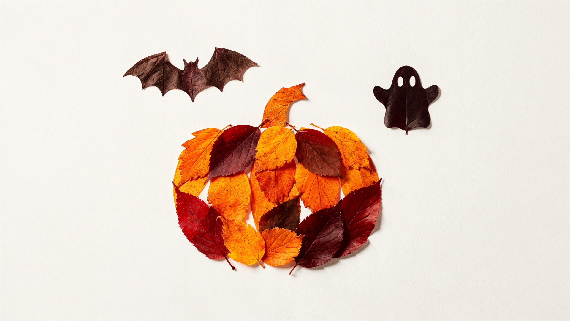 Minimal Halloween 4K Ultra HD PC desktop wallpaper: pumpkin made of orange, red and brown leaves, flanked by a bat and a small ghost cutout on a white background.