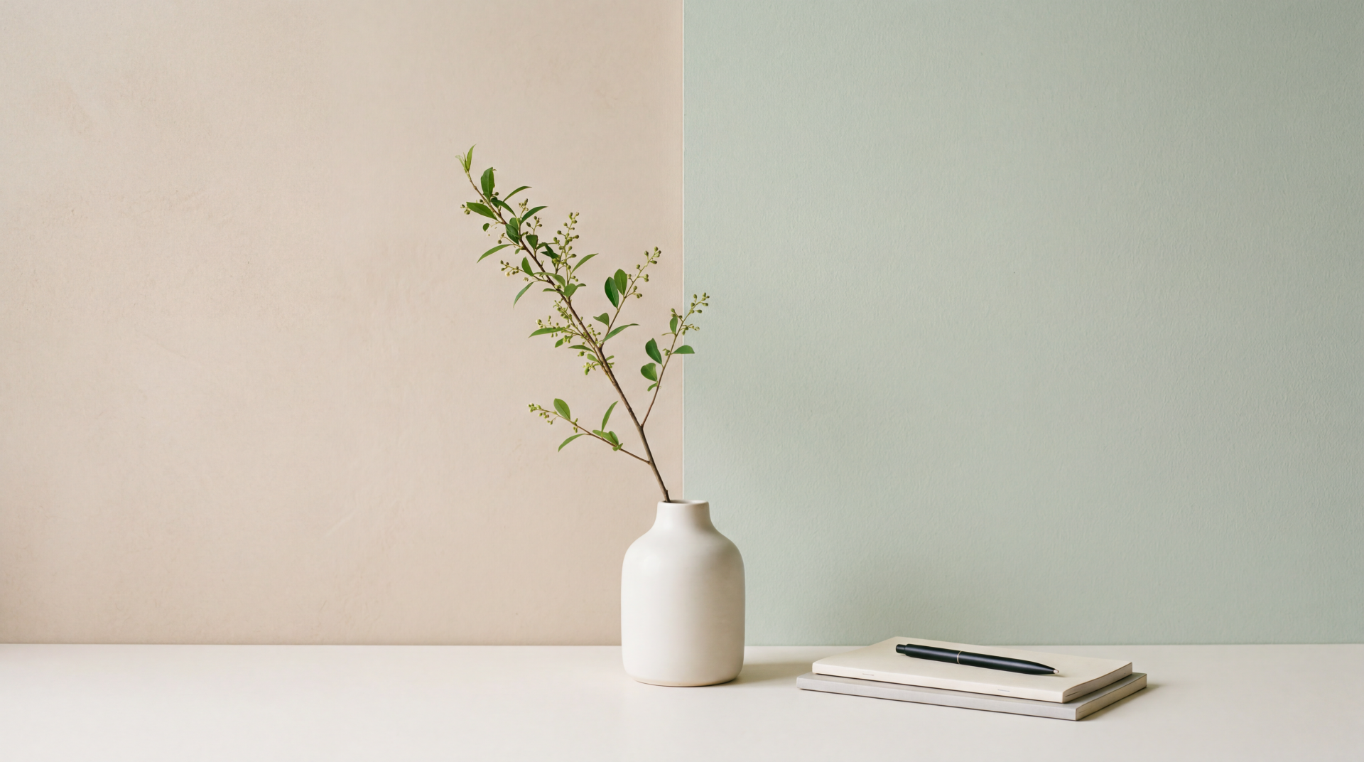 Clean 5K Ultra HD PC desktop wallpaper: minimalist white vase holding a slender leafy branch against a soft two-tone background, with a notebook and pen resting on the pale surface.