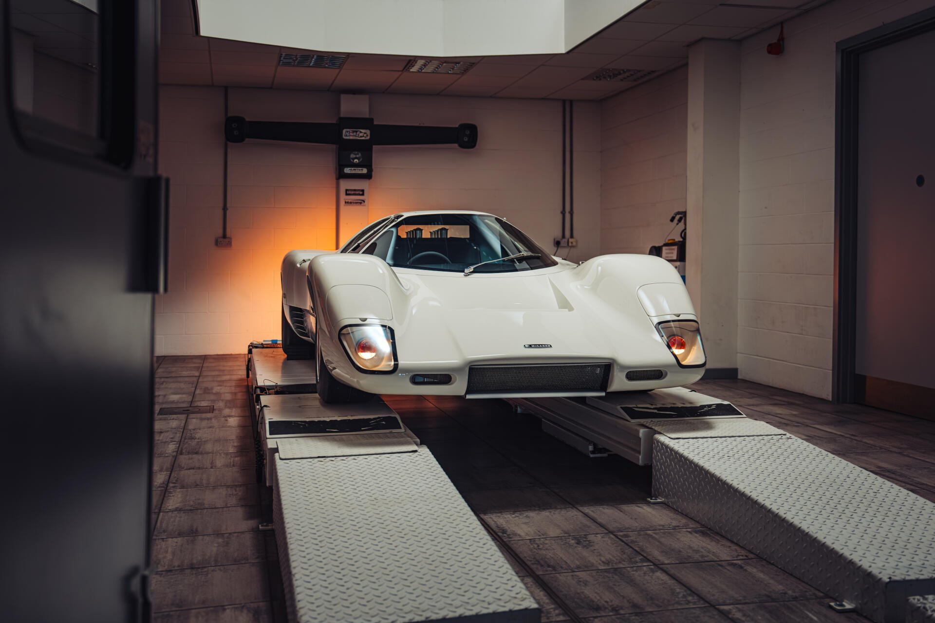 White McLaren G6GT vehicle on a garage lift, shown in 8K Ultra HD as a PC desktop wallpaper/background.