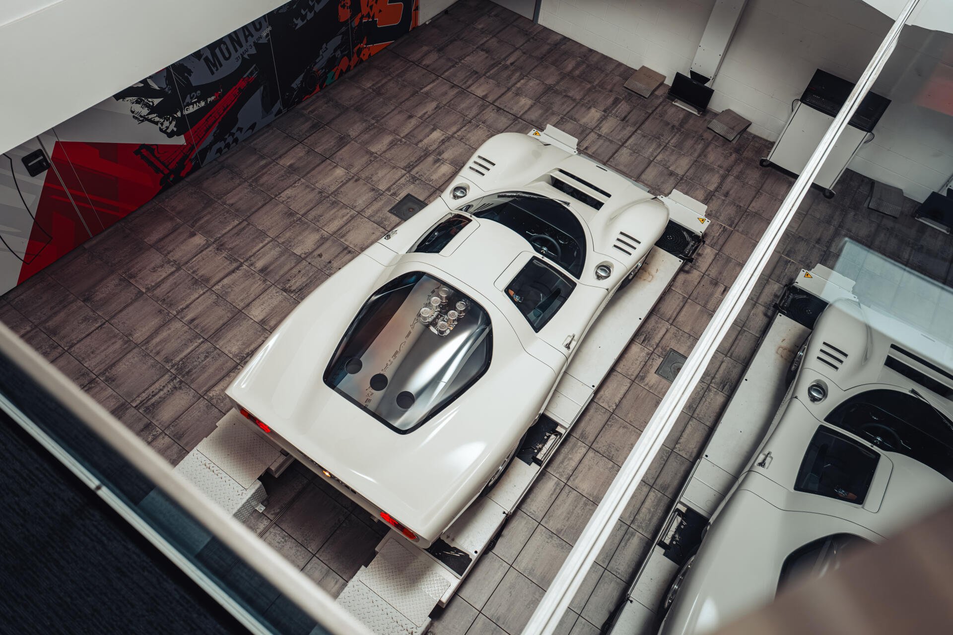 Overhead view of a white McLaren G6GT in a showroom bay, mirrored in adjacent glass — high-resolution 8K Ultra HD vehicle desktop wallpaper and background.