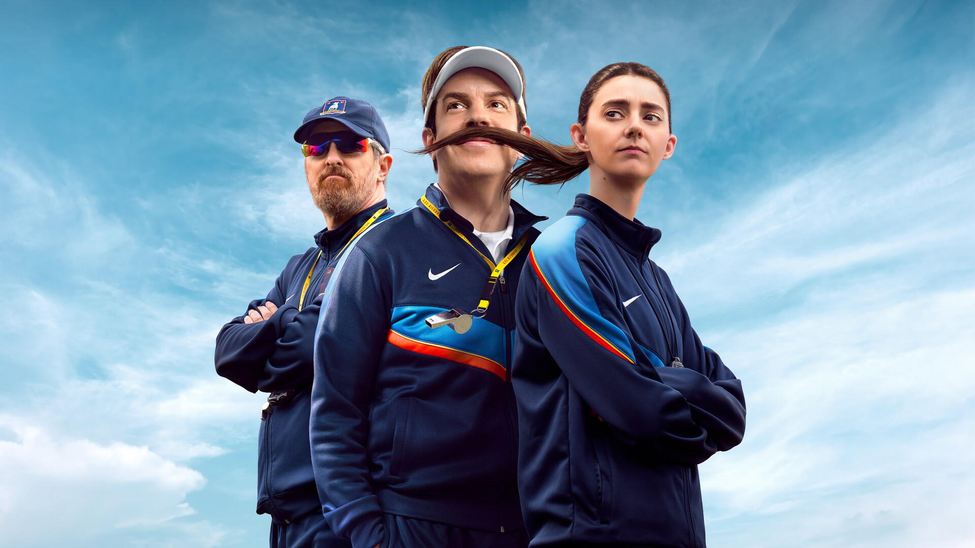 4K Ultra HD PC desktop wallpaper: three coaches in navy tracksuits in a Ted Lasso–inspired pose, mustached coach center, arms-crossed teammates against a bright cloudy sky.