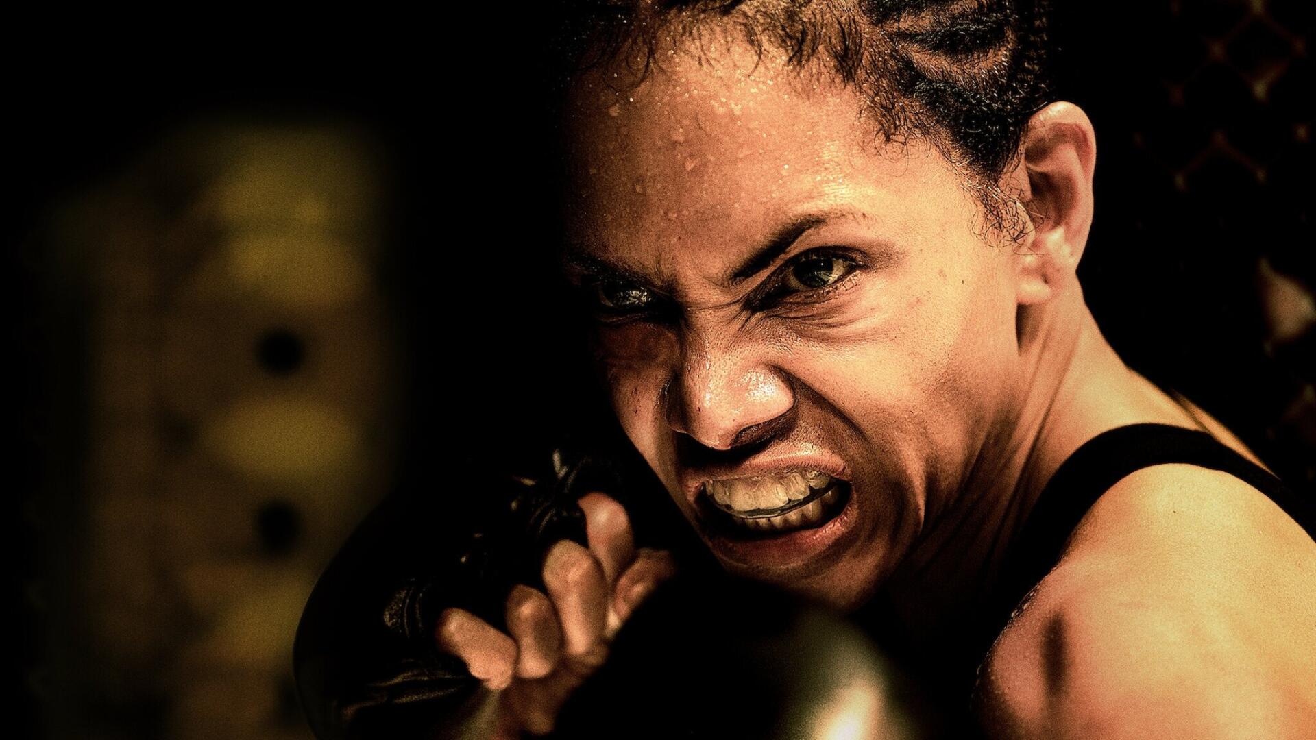 HD PC desktop wallpaper: bruised female fighter in close-up, snarling and clenching a gloved fist, sweat and grit on her face conveying fierce battle intensity.