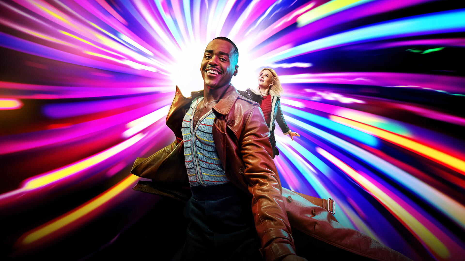Doctor Who (2023) 4K Ultra HD PC desktop wallpaper: smiling Doctor in a brown coat and a companion racing through a vivid, multicolored time‑vortex of light.