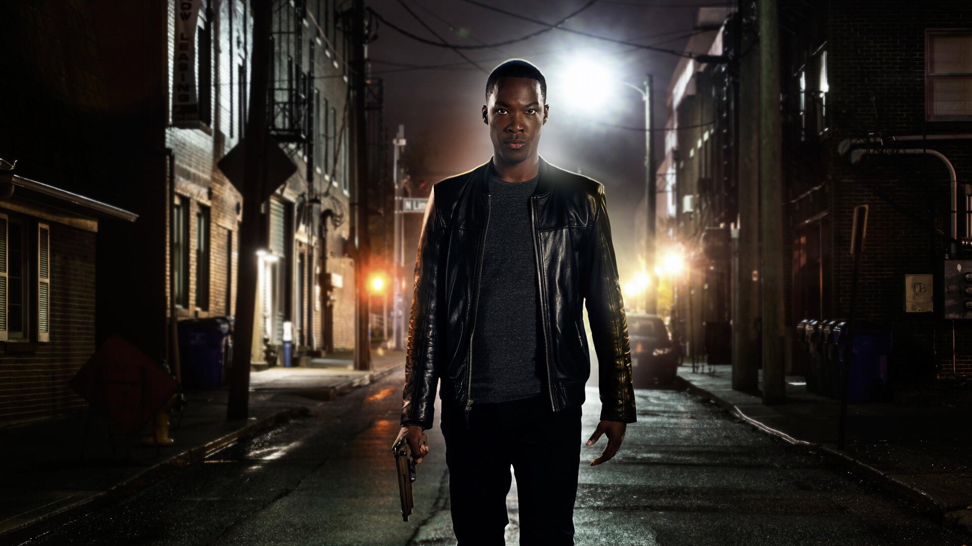 24: Legacy — 4K Ultra HD PC desktop wallpaper: a lone man in a leather jacket walks down a dim, rain-slick city alley at night, backlit by car headlights, holding a handgun.