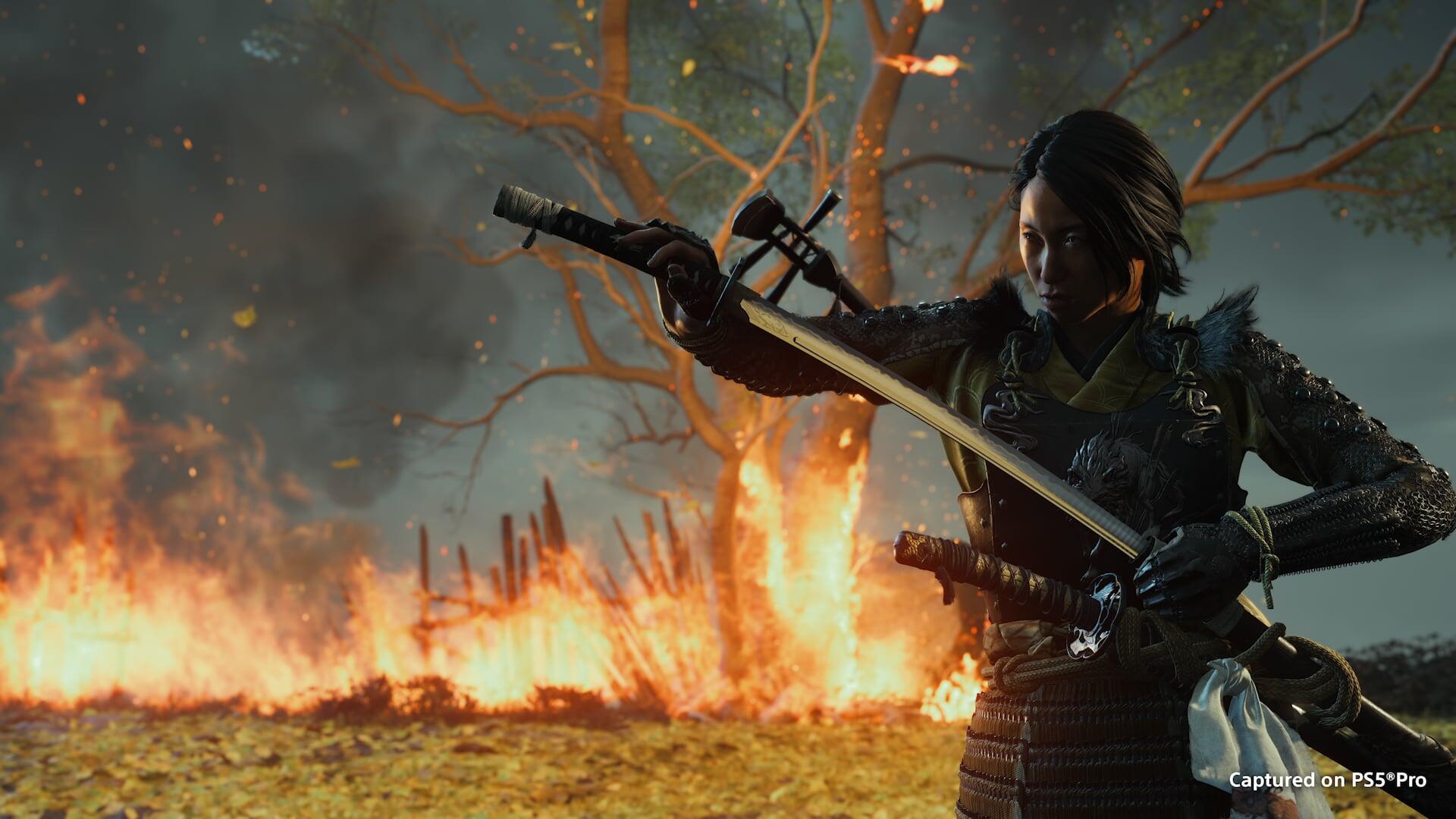 HD PC desktop wallpaper: Ghost of Yōtei samurai warrior drawing a katana amid a burning battlefield and twisted tree, cinematic video game background.