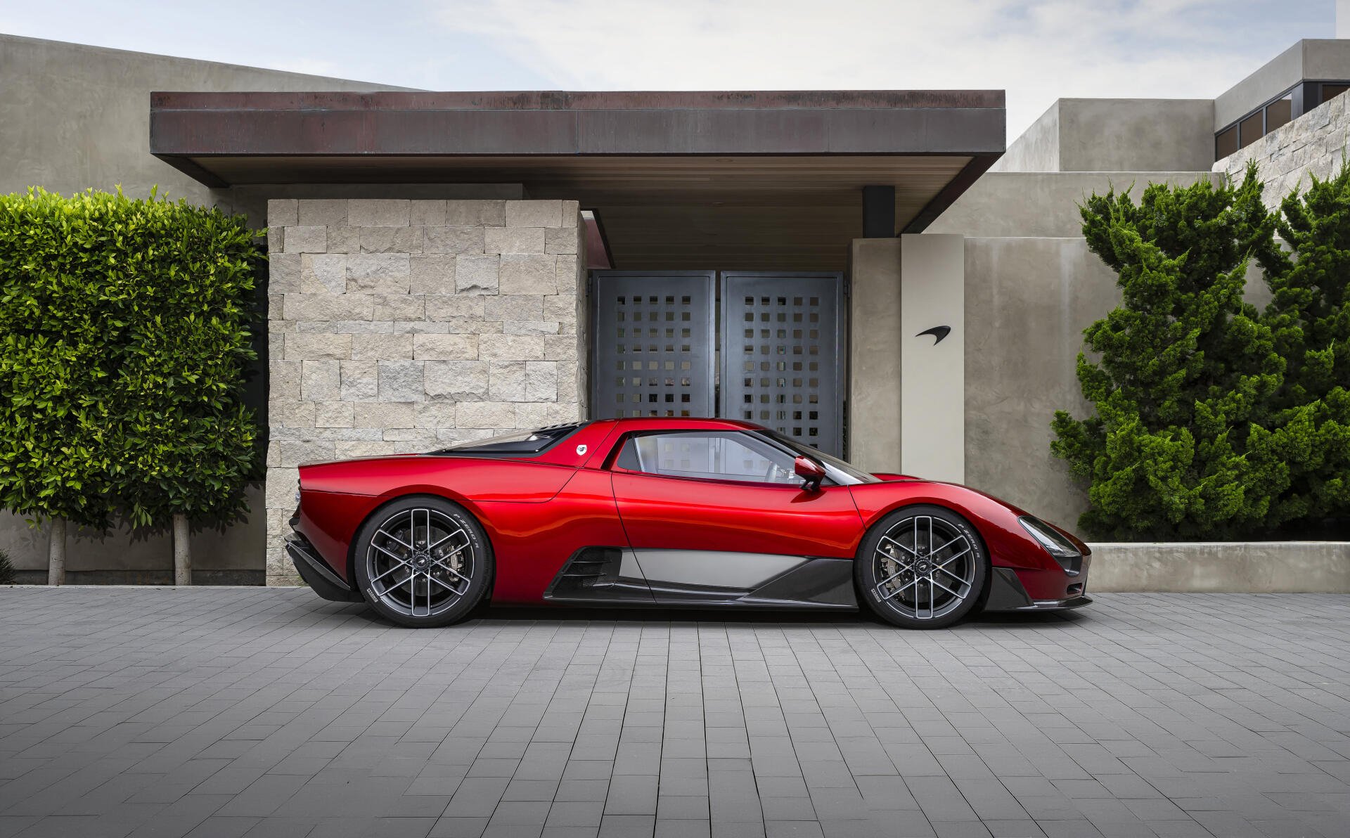 Side profile of a red McLaren McL 6GT sports car parked in front of a modern house; 8K Ultra HD PC desktop wallpaper/background.