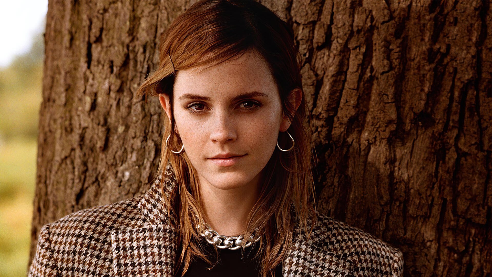 Close-up portrait of a young woman in a houndstooth coat with hoop earrings leaning against a tree — 2K Quad HD PC desktop wallpaper/background.