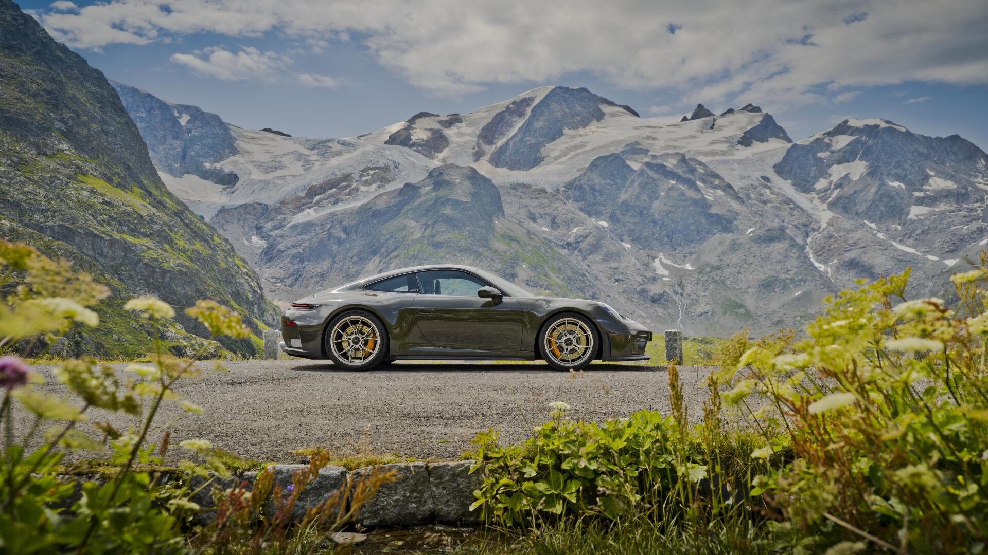 Side profile of a Porsche 911 GT3 sports car parked on a mountain road, 5K Ultra HD PC desktop wallpaper with alpine peaks and wildflowers.