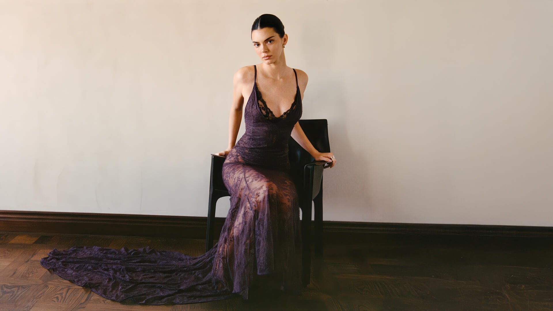 Female model in a sheer floor-length dark gown seated on a chair against a plain wall — 5K Ultra HD PC desktop wallpaper.