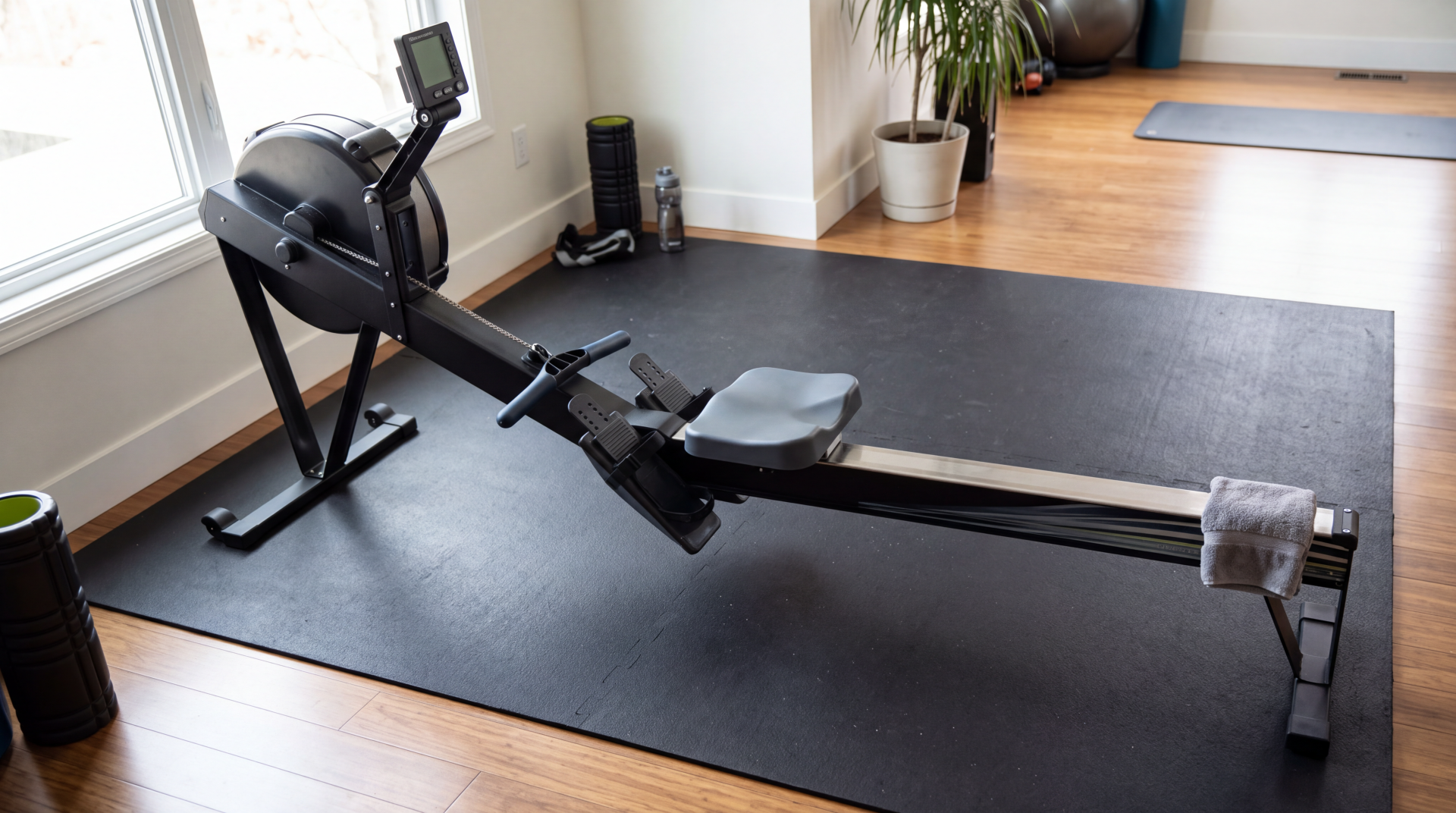 Rowing machine on a black mat in a bright home gym, 5K Ultra HD PC desktop wallpaper and background.