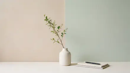 Clean 5K Ultra HD PC desktop wallpaper: minimalist white vase holding a slender leafy branch against a soft two-tone background, with a notebook and pen resting on the pale surface.