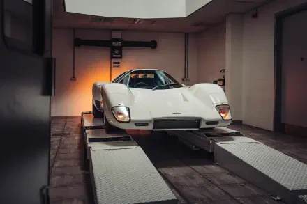 White McLaren G6GT vehicle on a garage lift, shown in 8K Ultra HD as a PC desktop wallpaper/background.