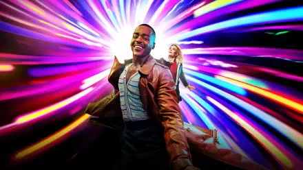 Doctor Who (2023) 4K Ultra HD PC desktop wallpaper: smiling Doctor in a brown coat and a companion racing through a vivid, multicolored time‑vortex of light.