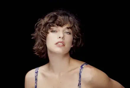 2K Quad HD PC desktop wallpaper: close-up portrait of a woman with short curly hair and tousled bangs, bare shoulders, soft lighting against a black background.