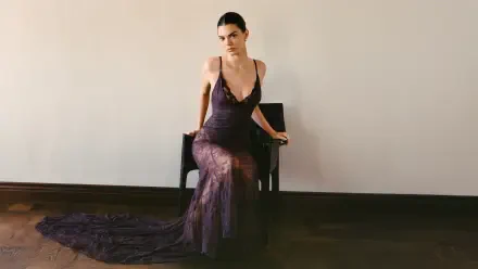 Female model in a sheer floor-length dark gown seated on a chair against a plain wall — 5K Ultra HD PC desktop wallpaper.