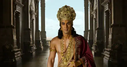 Actor in Ramayana (2026) as a royal king wearing an ornate gold crown and red cloak in a palatial corridor — 4K Ultra HD PC desktop wallpaper background.