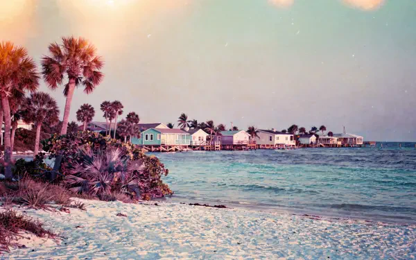 Florida beach at sunrise with palms, pastel sky and turquoise water, coastal cottages on the horizon — 4K Ultra HD PC desktop wallpaper and background.