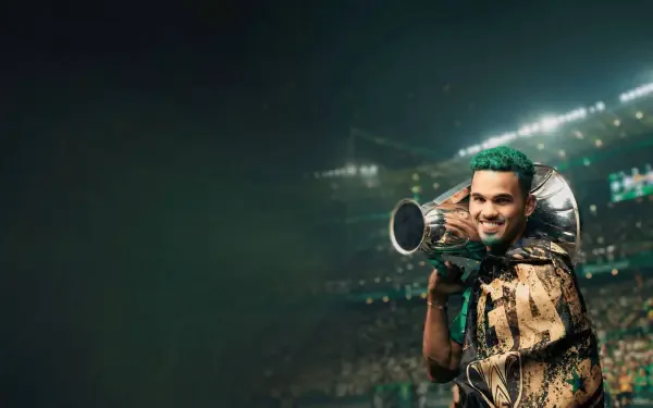 HD PC desktop wallpaper of an Al Ahli Saudi Pro League player in club green, smiling and holding a trophy-like megaphone amid stadium lights and a cheering crowd.