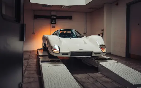 White McLaren G6GT vehicle on a garage lift, shown in 8K Ultra HD as a PC desktop wallpaper/background.