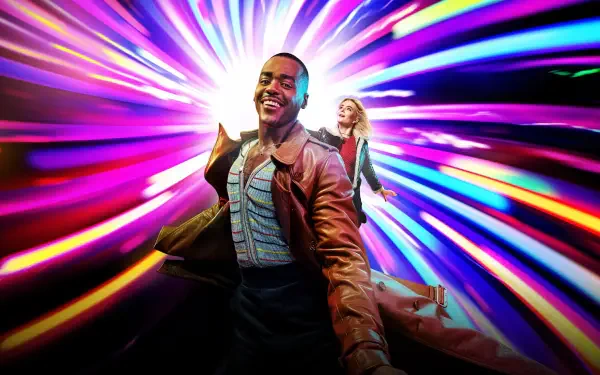 Doctor Who (2023) 4K Ultra HD PC desktop wallpaper: smiling Doctor in a brown coat and a companion racing through a vivid, multicolored time‑vortex of light.