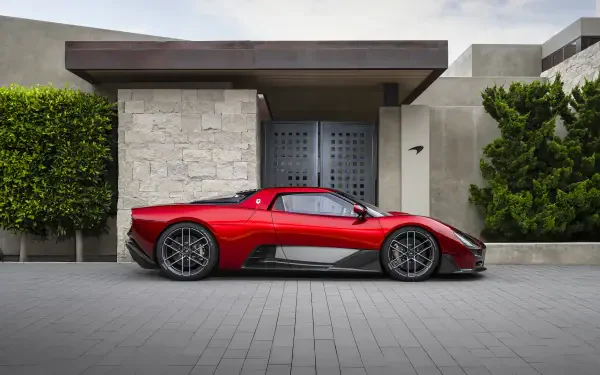 Side profile of a red McLaren McL 6GT sports car parked in front of a modern house; 8K Ultra HD PC desktop wallpaper/background.