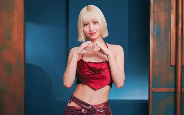 5K Ultra HD desktop wallpaper: blonde woman with a short bob in a red satin crop top and low-rise pants, making a heart with her hands—K-pop–inspired styling against a blue-copper studio backdrop.