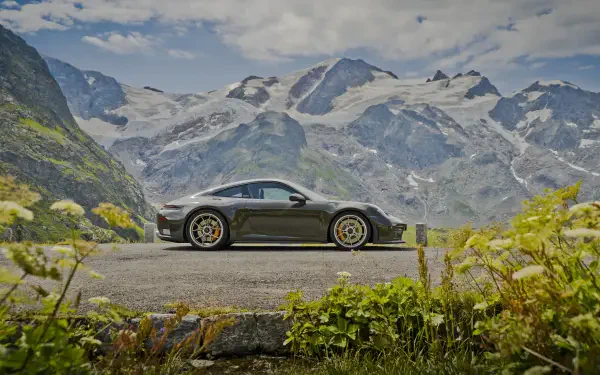 Side profile of a Porsche 911 GT3 sports car parked on a mountain road, 5K Ultra HD PC desktop wallpaper with alpine peaks and wildflowers.