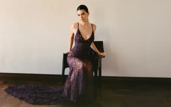 Female model in a sheer floor-length dark gown seated on a chair against a plain wall — 5K Ultra HD PC desktop wallpaper.