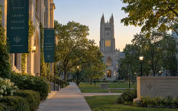4K Ultra HD PC desktop wallpaper and background: university college campus at dusk, tree-lined walkway leading to a cathedral-style building with banners and manicured lawns.