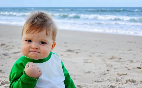 Fist-pumping baby meme with a triumphant expression on a sandy beach, classic success-meme vibe; 4K Ultra HD PC desktop wallpaper/background.