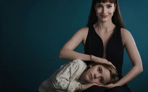 Other Mommy (2026) 2K Quad HD PC desktop wallpaper featuring a woman in black with a child resting on her lap against a dark teal background.