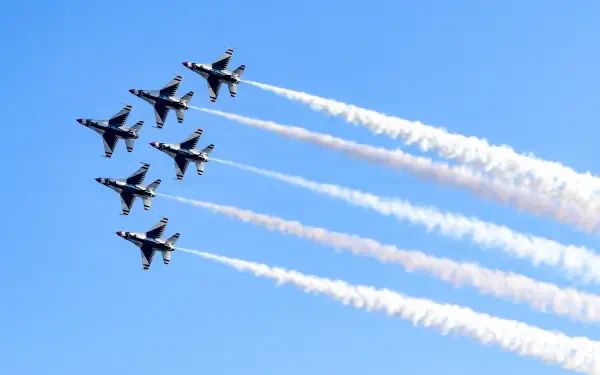 United States Air Force Thunderbirds F-16 Fighting Falcons soar in formation, trailing white smoke across a blue sky in 5K Ultra HD desktop wallpaper.