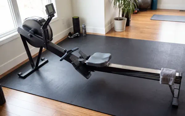 Rowing machine on a black mat in a bright home gym, 5K Ultra HD PC desktop wallpaper and background.